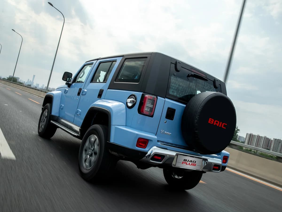 Sky Blue BAIC BJ40 Plus from behind on a highway, showing the rear recovery hooks and spare wheel