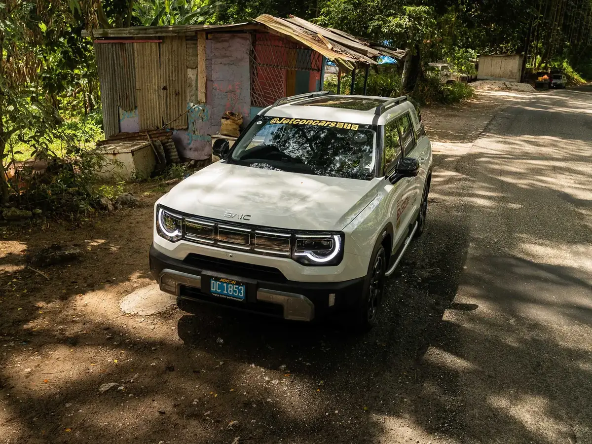 White BAIC BJ30e on a shaded Jamaican country road, seen from a high front three-quarter angle